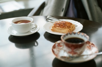 面包放在陶瓷盘子里，靠近装满咖啡的白色陶瓷茶杯